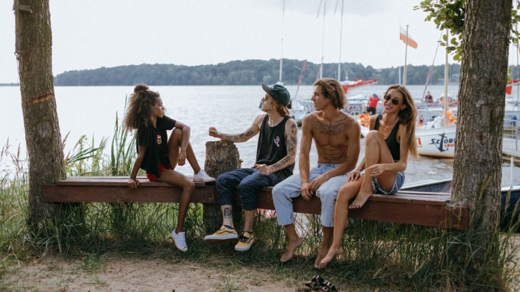 A diverse group of friends enjoying leisure time by a picturesque lakeside with boats in the background.